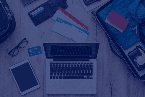 A top-down shot reveals a laptop, tablet, and smartphone alongside boarding passes, wallets, glasses, and a packed suitcase on a light wooden surface. The arrangement conveys a sense of preparation for a journey, blending technology with traditional travel items. The open laptop and other devices suggests planning and connectivity on the go. The photo's bright lighting and organized composition lends itself well to concepts such as travel planning, digital nomadism, technology integration, and vacation preparation. Its neutral tones and clear imagery make it suitable for use in travel blogs, technology websites, or marketing materials for travel agencies.
