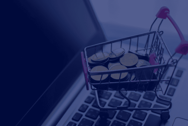 A miniature shopping cart filled with gold coins sits on a laptop keyboard in this close-up studio shot. The composition highlights the concept of online spending, digital transactions, and the ease of ecommerce. The muted lighting and modern laptop design creates a sophisticated feel, making this image ideal for conveying themes of financial technology, investments, digital marketing, and online commerce.
