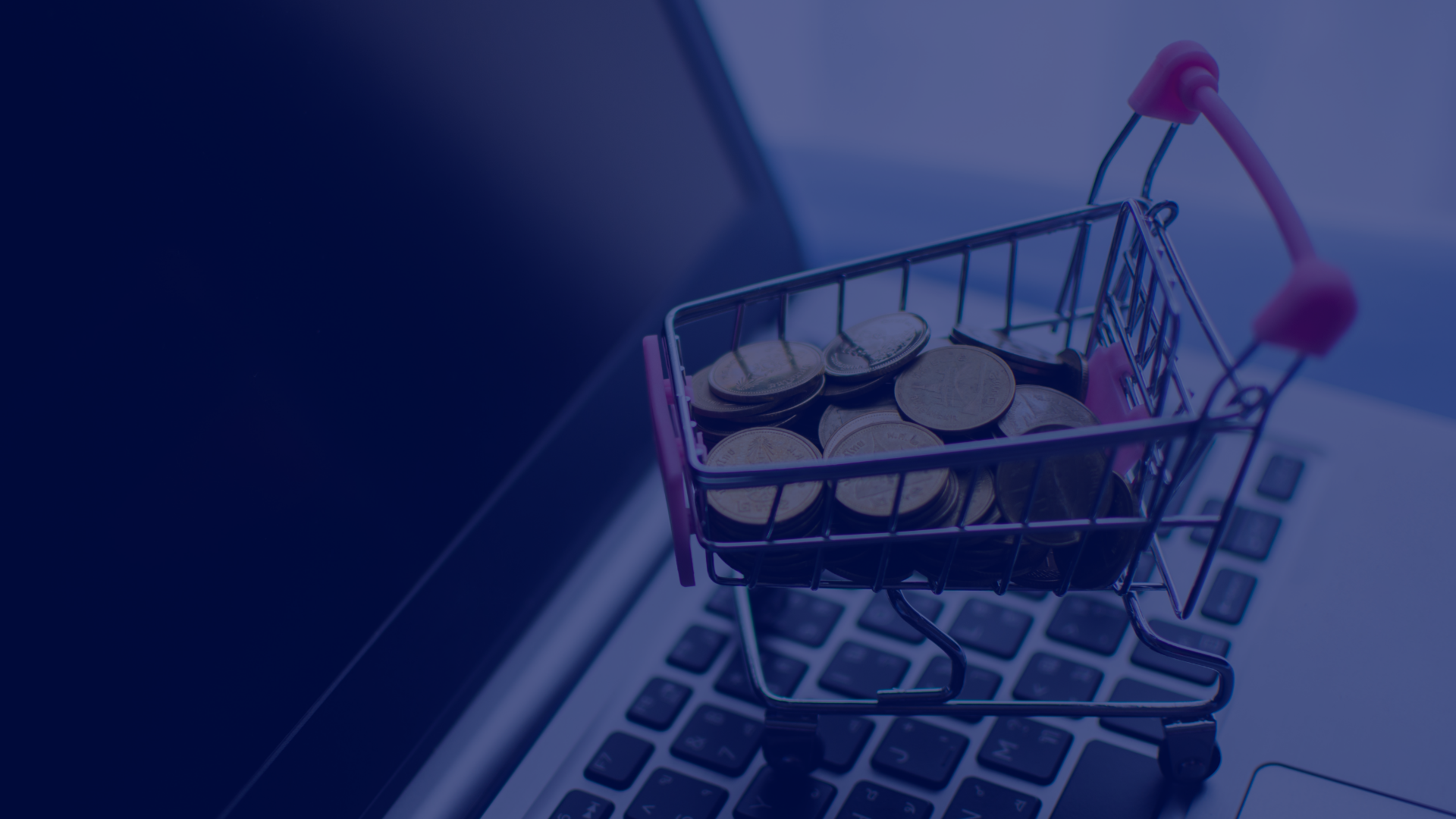 A miniature shopping cart filled with gold coins sits on a laptop keyboard in this close-up studio shot. The composition highlights the concept of online spending, digital transactions, and the ease of ecommerce. The muted lighting and modern laptop design creates a sophisticated feel, making this image ideal for conveying themes of financial technology, investments, digital marketing, and online commerce.
