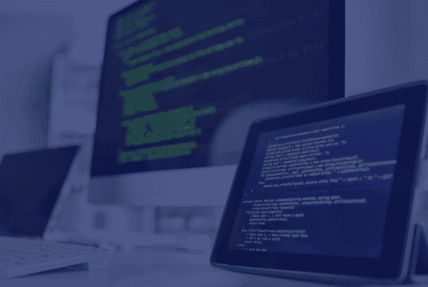This photo showcases a brightly lit office setting, dominated by a computer and tablet displaying lines of code. A partially visible laptop and keyboard suggest a workspace focused on technology. The setup, against a blurred backdrop, evokes a modern and professional atmosphere. This image is ideal for projects centered on programming, software development, or digital workspaces, embodying themes of innovation, precision, and technological advancement.