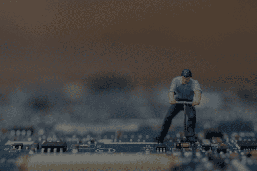 A tiny figurine of a man with short brown hair, wearing a blue short-sleeved shirt, dark trousers and a blue baseball cap, uses a tool on a blue circuit board. He is a product engineer. The image evokes the idea of fixing or inspecting computer or technology components. The background is out of focus. The mood is serious and analytical. This photo could be used for illustrative purposes in business or educational materials about technology, engineering, or innovation.